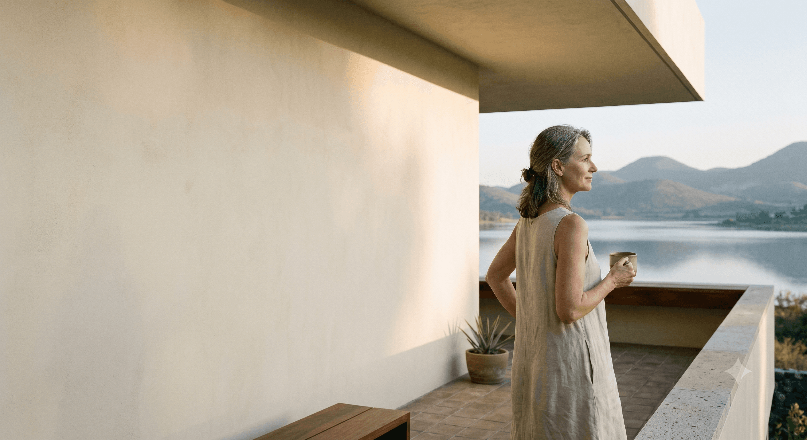 A modern home terrace above Lake Chapala at dawn, a woman looking out at the water with a cup of coffee